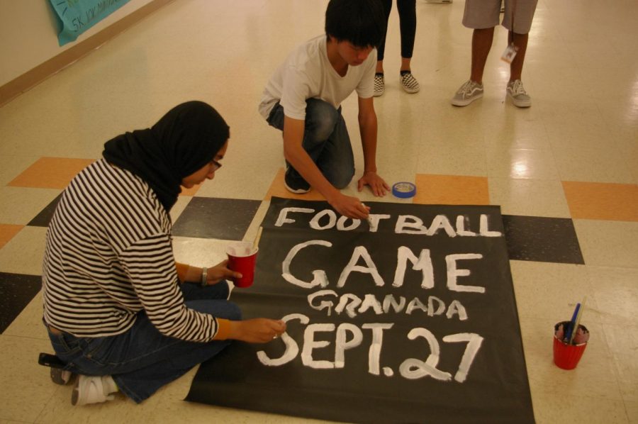 From left to right, freshman leadership students Alizay Iqbal and Christopher Chiang paint a poster to advertise the football game that took place on Sept. 27.