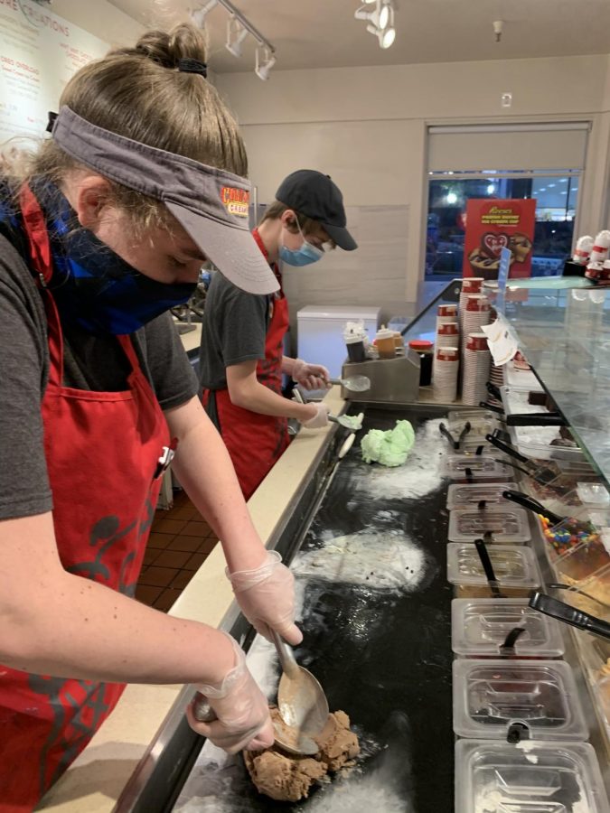 A Cold Stone employee dons gloves and a face mask before constructing an ice cream concoction for a customer.