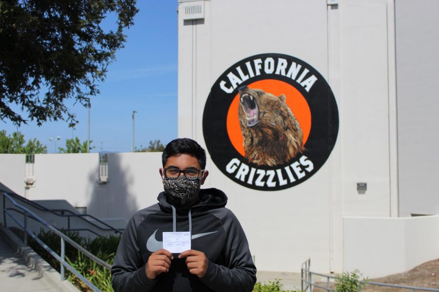 Cal High junior Jonah Aziz stands in front of Cal High holding his COVID-19 vaccination card.
