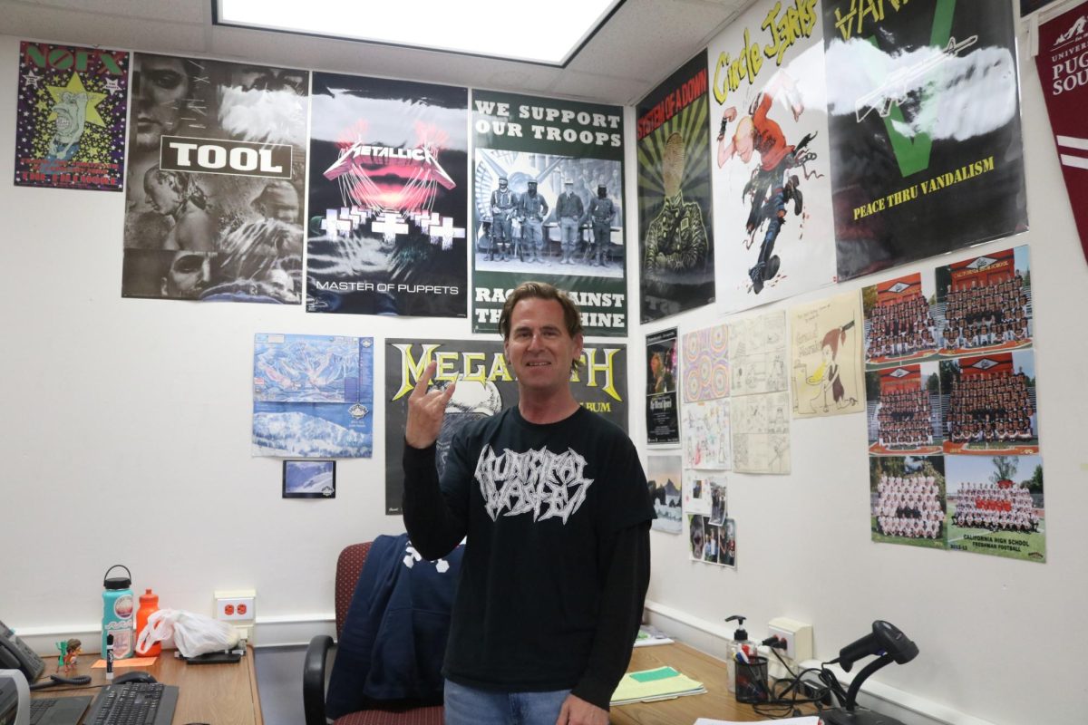 Joseph+Sussman+poses+with+his+metal+posters.+Sussman+plays+the+bands%E2%80%99+music+to+wake+up+his+students+when+class+starts.