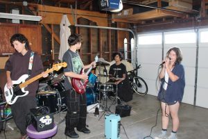 Members of the band Friendly Fire get ready for their next gig by rehearsing in drummer Lucas Chan’s garage. Other band members include bassist Orion Duerrmeier, left, guitarist Mojo Maldonado, center, and singer Viktoria Lutsenko.