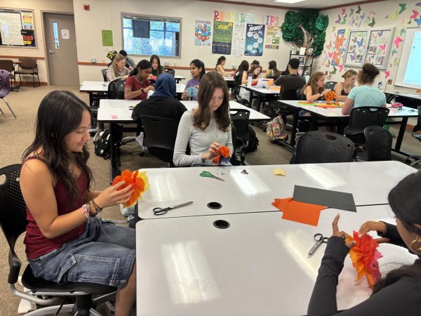 Senior Ava Ryan, left, and junior Scarlett Scorsonelli add the final touches of their paper marigolds for Hispanic heritage month during a student support class offered in the library.