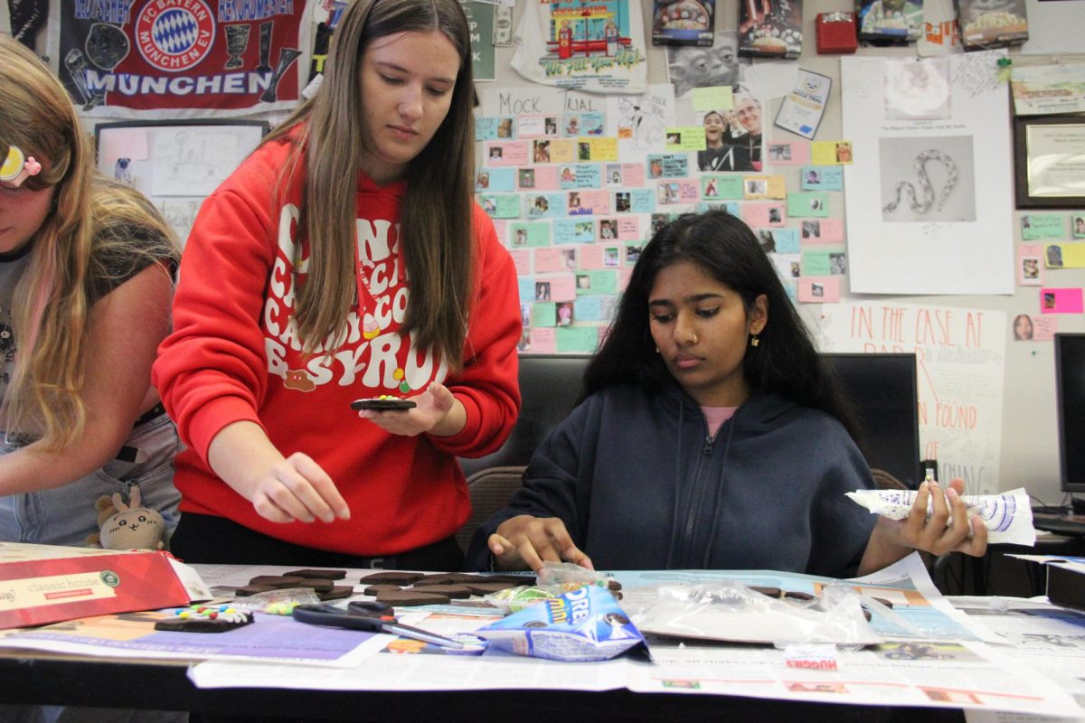 Seniors Olivia Soares, left, and Mansi Swaminathan assemble their team's gingerbread house during the newspapers annual gingerbread house making competition.
